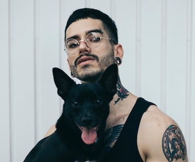 hipster man with short hair tattoos and a black dog