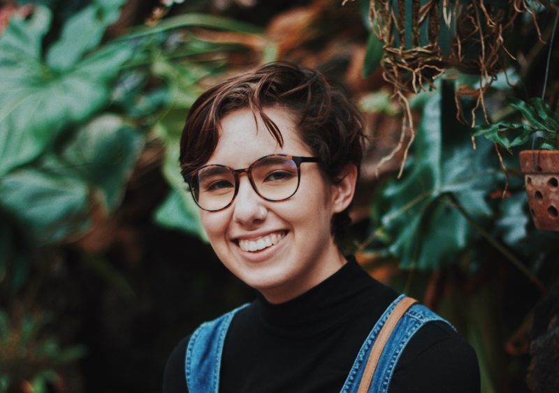 Person with short hair smiling standing in front of trees