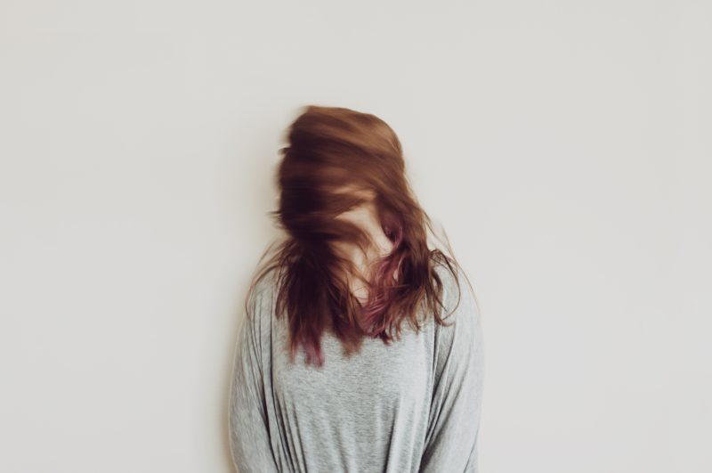 Person with long read hair in a gray sweater and background eith the face hidden 